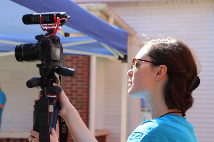 Ellie standing behind a video camera on a tripod